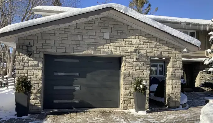 A garage beside a large stone wall, with a blanket of snow covering the ground.
